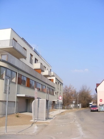 Moderní bytový dům Pod Tyršovým vrchem s balkóny na rohu klidné ulice za slunečného dne.