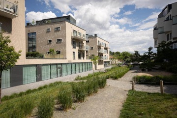 Moderní bytové domy s terasami v zeleni za slunečného dne.