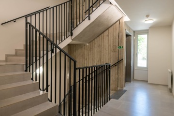 Schodiště obytného domu s vnitřním kovovým zábradlím.