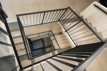 Schodiště obytného domu s vnitřním kovovým zábradlím.