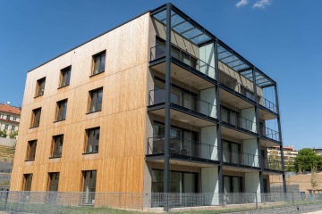 Moderní dřevěná budova s balkonovými terasy na ocelové konstrukci.