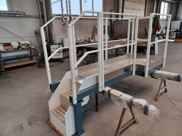 Kovové schodiště s protiskluzovou úpravou v dílně, zavěšené na řetězech.