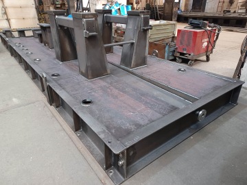 Ocelová konstrukce v průmyslové dílně s červeným elektrickým zařízením na podlaze.