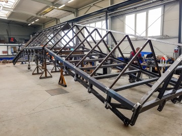 Stavební kovová konstrukce v dílně s mužem, který pracuje na montáži.