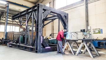 Svářeč pracuje na kovové konstrukci ve velké průmyslové hale.