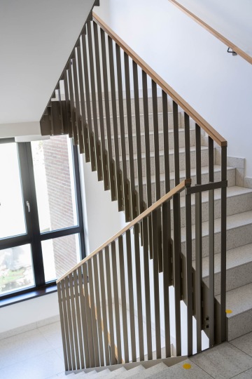 Schodiště Marina Nova s kovovým zábradlím a dřevěným madlem, vedle okna s okenicemi.