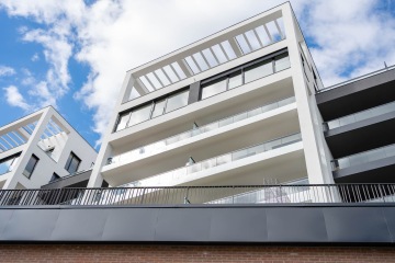 Moderní bytová budova Marina Nova s bílými balkony a skleněným zábradlím pod modrou oblohou.