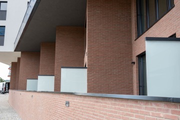 Cihlová fasáda moderní budovy Marina Nova s balkony a matnými skleněnými zábranami.
