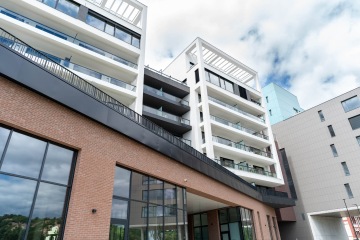 Moderní bytový dům Marina Nova s cihlovou fasádou a prosklenými balkony pod modrou oblohou.