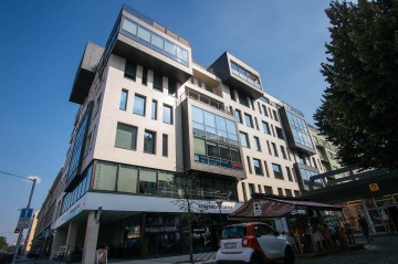 Moderní kancelářská budova s prosklenými fasádami, Starbucks v přízemí, zaparkované auto, modrá obloha.