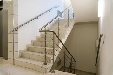 Moderní vnitřní schodiště s nerezovým zábradlím a světlými dlaždicemi.