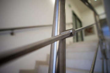 Nerezové zábradlí na schodišti s rozmazaným pozadím schodů.