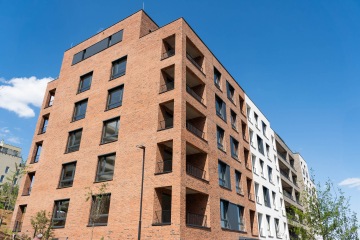 Moderní cihlový bytový dům projektu Nová Waltrovka s balkony pod modrou oblohou.