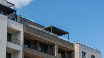 Moderní bytový dům projektu Nová Waltrovka s terasou a skleněným zábradlím pod modrou oblohou.