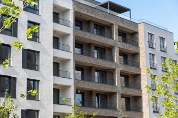 Moderní bytový dům projektu Nová Waltrovka s balkony a cihlovou fasádou za slunečného dne.