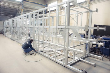 Technik pracuje na konstrukci z ocelových rámů v hale.