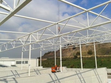 Stavba ocelové konstrukce s jeřábem na zeleném pozadí.