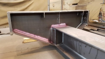 Ocelový nosník s růžovou kontrolní barvou v dílně.