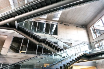 Moderní interiér s geometrickým točitým schodištěm s ocelovou konstrukcí a celoskleněným zábradlím.