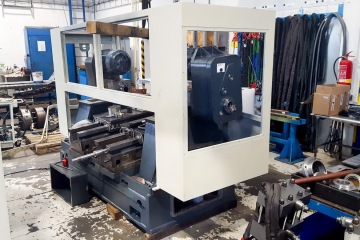 CNC stroj v dílně s nástroji a ochranným krytem, obklopen náhradními díly a vybavením.