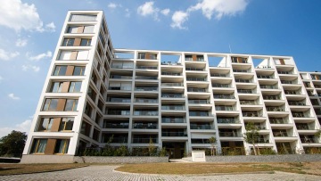 Moderní bytový dům s balkony pod modrou oblohou.