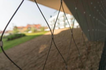 Detail ocelového pletiva s rozostřeným pozadím městského prostředí.