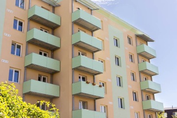 Šestipatrový bytový dům se slunečnými lodžiemi v pastelových barvách za slunečného dne.