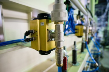 Průmyslové ventily a trubky s modrými kabely v řadě na výrobní lince.