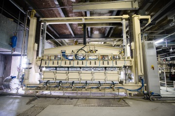 Průmyslový stroj s trubkami a kabely v tovární hale.