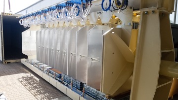 Modulární zařízení s několika kovovými a plastovými součástmi umístěné vedle otevřeného kontejneru.