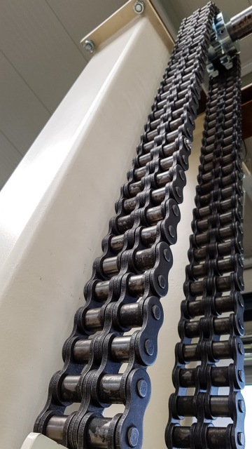 Řetěz dopravníku upevněný na kovovém nosníku ve skladu.