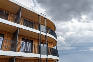 Moderní dřevěná fasáda zakřivené budovy Timber proti zatažené obloze.