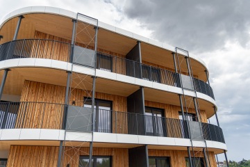 Moderní dřevěná budova Timber se zaoblenými balkóny pod zamračenou oblohou.