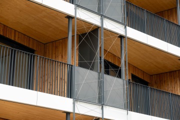 Balkóny moderní budovy Timber s dřevěnými stěnami a kovovými zábradlími.