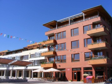 Moderní budova Dolní Břežany s terasami, barevnými praporky a venkovním posezením za slunečného počasí.