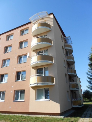 Pětipatrový bytový dům se zaoblenými balkony, modrá obloha.