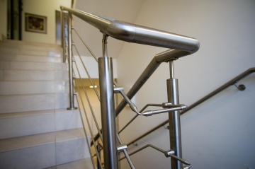 Vnitřní nerezové zábradlí na schodišti s porcelánovými dlaždicemi v interiéru.