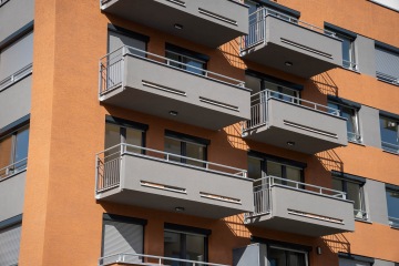 Moderní budova s oranžovou omítkou a šedými balkony v slunečném počasí.