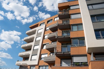 Moderní bytový dům s balkony na pozadí modré oblohy s mráčky.