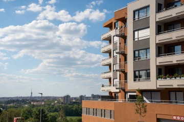 Moderní bytový dům s balkony a modrou oblohou v pozadí.