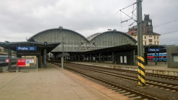 Praha hlavní nádraží s kolejemi, velkou prosklenou střechou a hodinovou věží v pozadí.